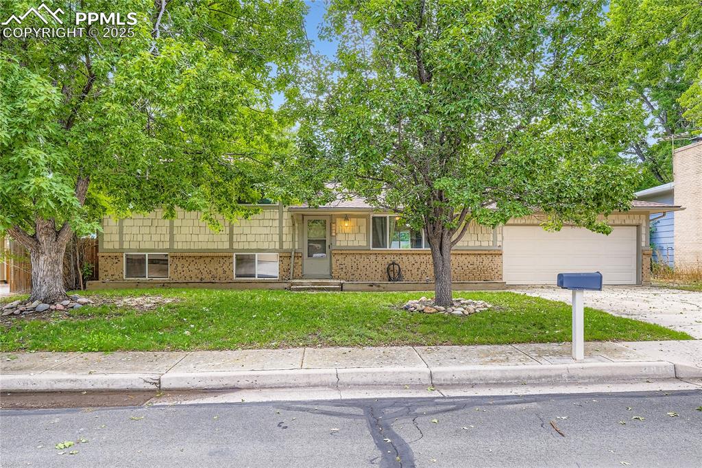 Caption: Tri-level home featuring brick siding, driveway, and a front lawn