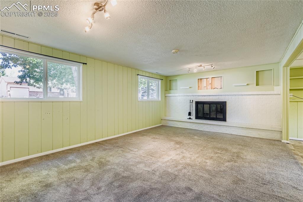 Image 18 of 28: Unfurnished living room with track lighting, a brick fireplace, a textured 