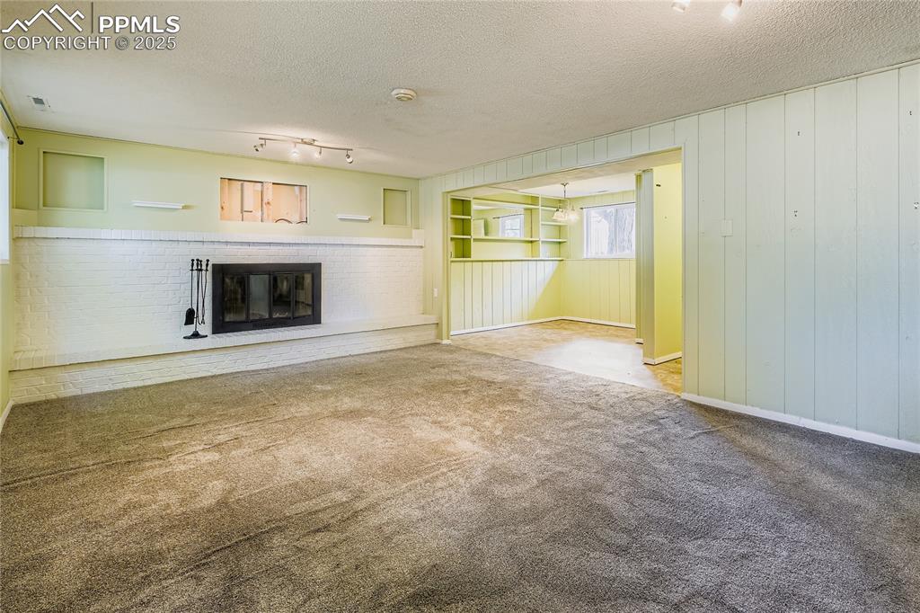 Image 19 of 28: Unfurnished living room featuring carpet, a textured ceiling, a fireplace, 