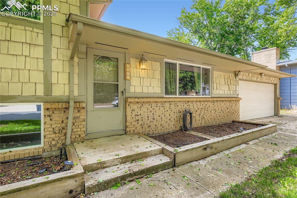 Image 3 of 28: Doorway to property with an attached garage and brick siding