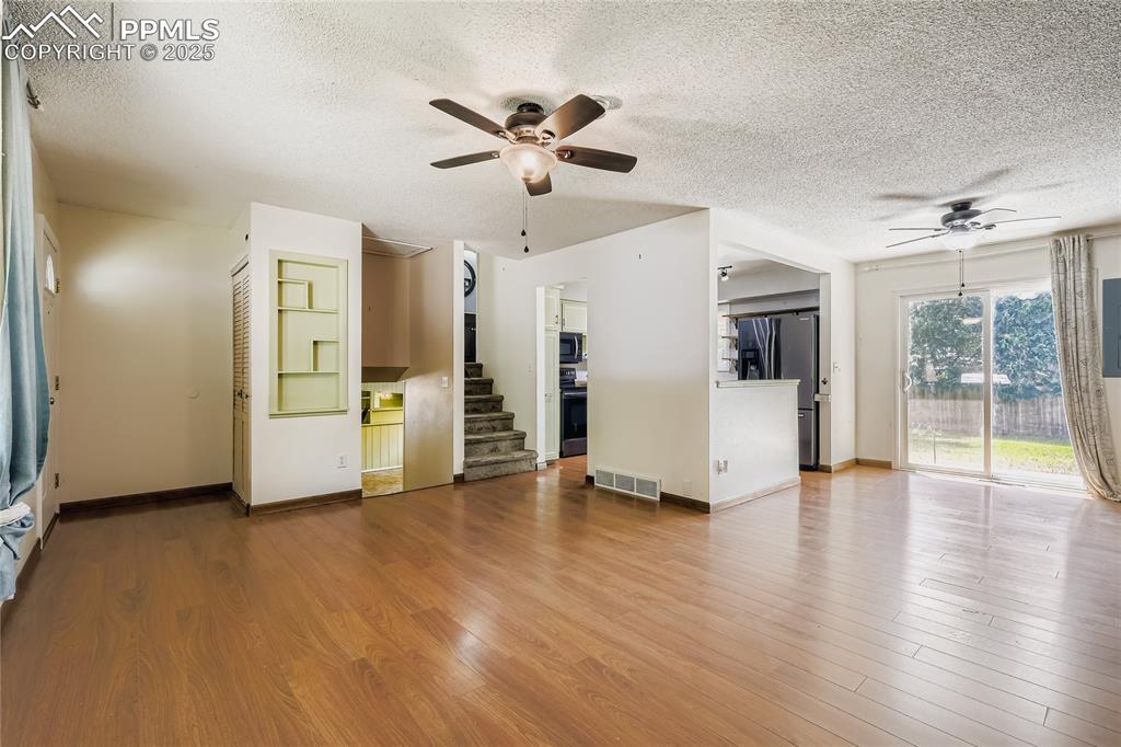 Image 7 of 28: Unfurnished living room with ceiling fan, wood finished floors, and a textu
