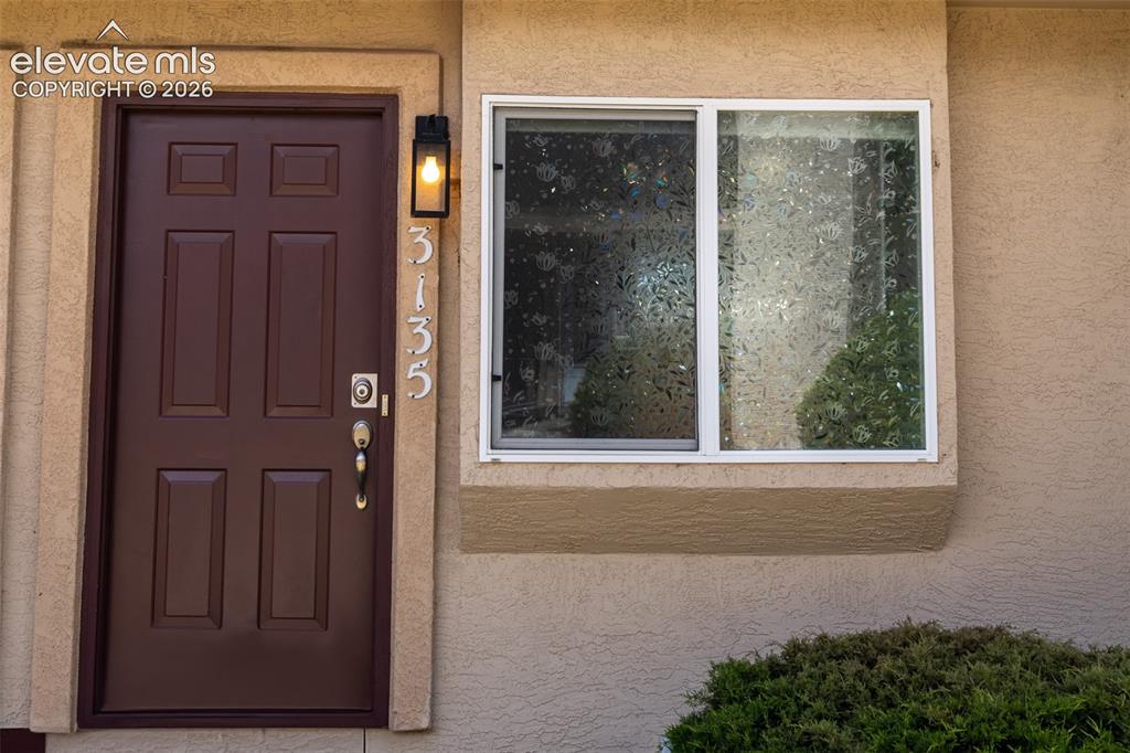Image 2 of 31: Entryway featuring a dark brown panel door with brass hardware, stucco exte