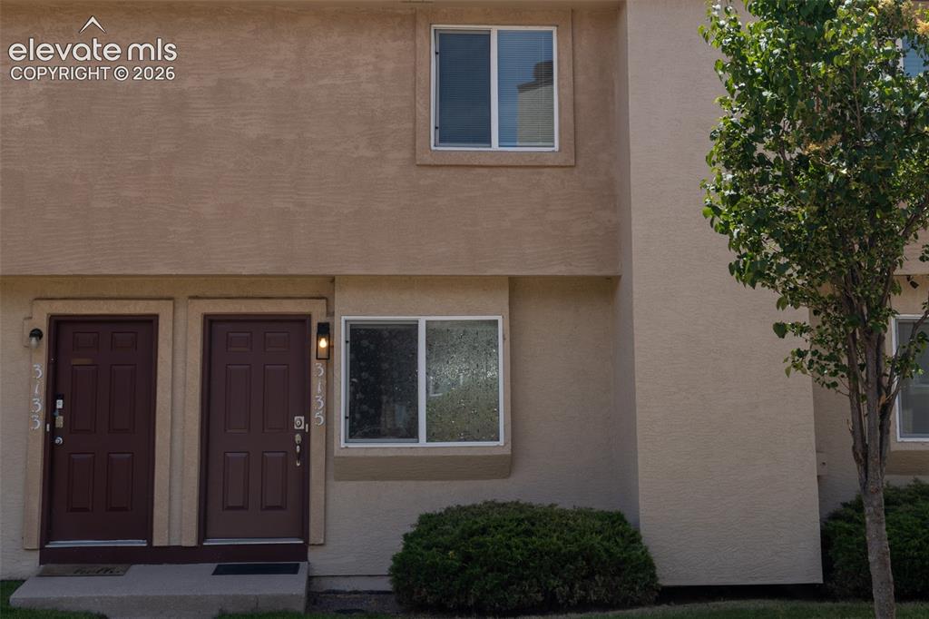 Image 26 of 31: Stucco exterior featuring two brown entry doors with exterior lighting fixt
