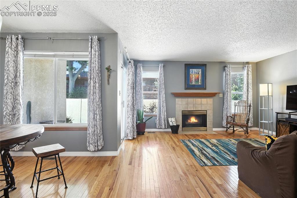 Image 11 of 25: Living room featuring a textured ceiling, wood-type flooring, and a firepla