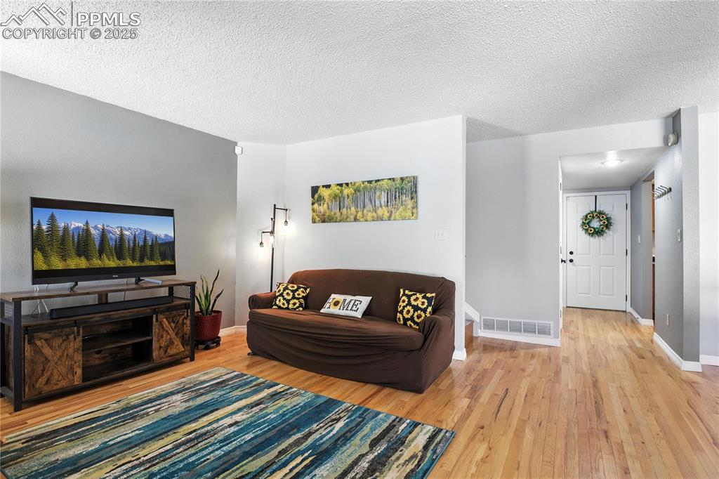 Image 7 of 25: Living area with light wood-type flooring and a textured ceiling