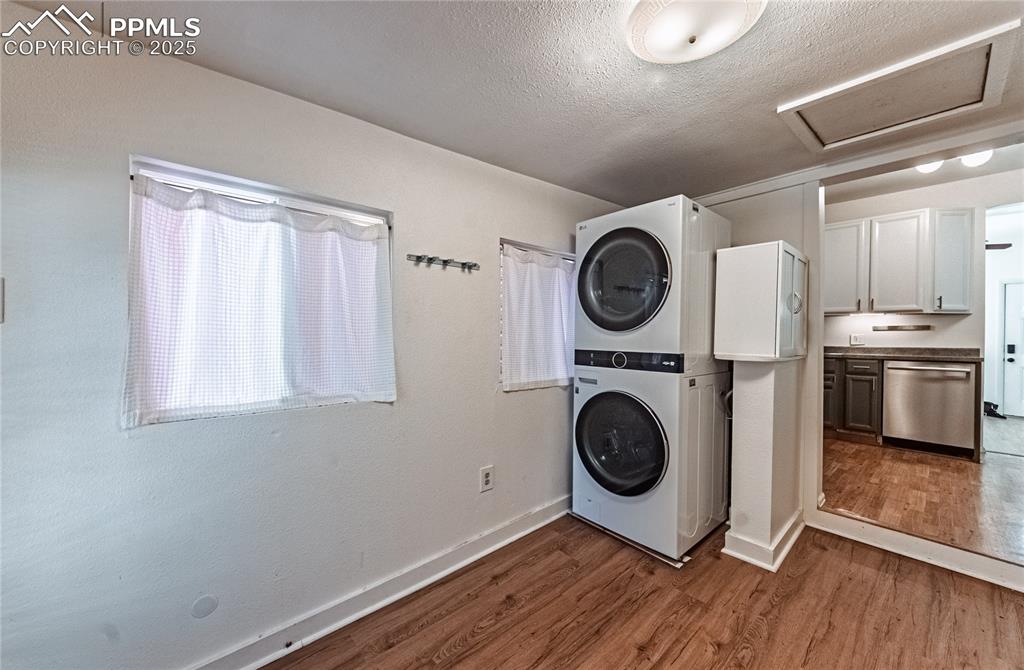 Image 27 of 36: Washroom with attic access, stacked washer / dryer, wood finished floors, a