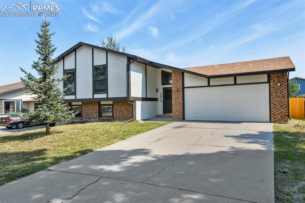 Caption: View of front of house with an attached garage, a front yard, driveway, stucco siding, and brick sid