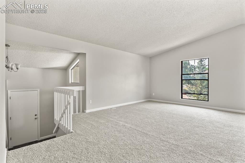 Image 10 of 39: Unfurnished room with a textured ceiling, carpet, vaulted ceiling, and a ch