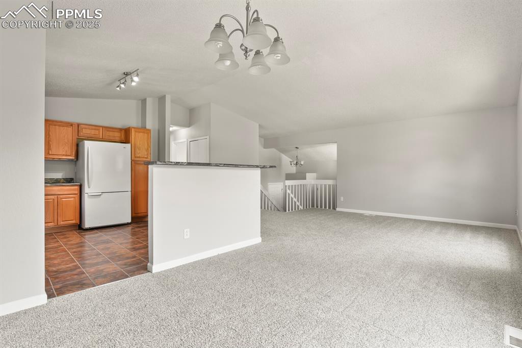 Image 11 of 39: Kitchen with lofted ceiling, a chandelier, dark carpet, freestanding refrig