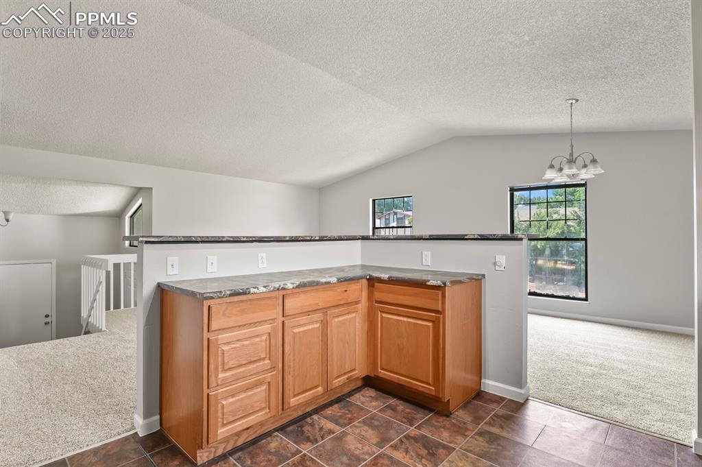 Image 14 of 39: Kitchen featuring a chandelier, lofted ceiling, a textured ceiling, dark co