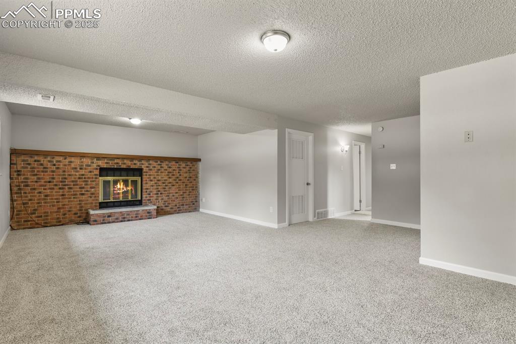 Image 23 of 39: Below grade area featuring a textured ceiling, a brick fireplace, and carpe