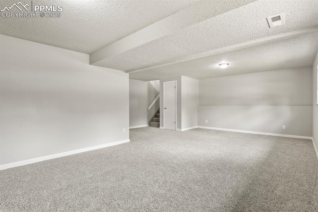 Image 25 of 39: Unfurnished room featuring a textured ceiling, stairs, and carpet