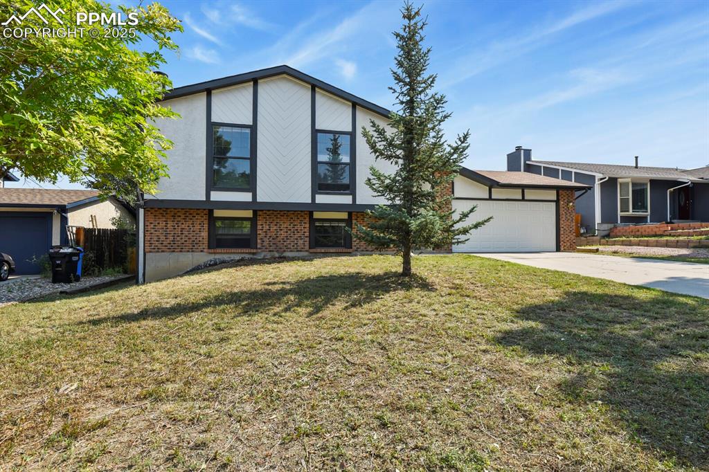 Image 4 of 39: View of front facade with brick siding, concrete driveway, and a front lawn