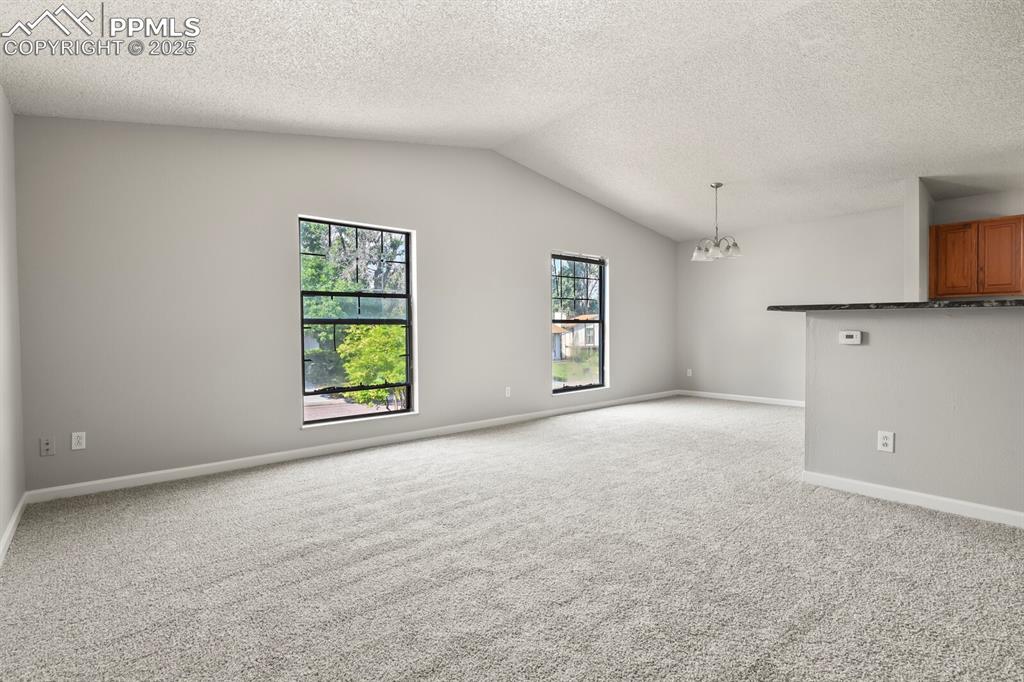 Image 7 of 39: Unfurnished room featuring vaulted ceiling, a chandelier, light carpet, and