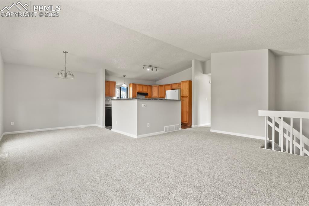 Image 8 of 39: Unfurnished living room featuring lofted ceiling, light carpet, a chandelie