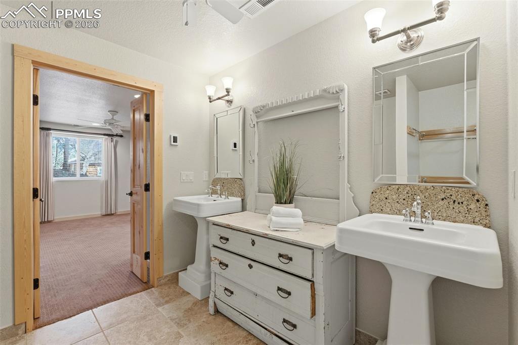 Image 30 of 50: Full bathroom with ceiling fan, two sinks, light colored carpet, light tile