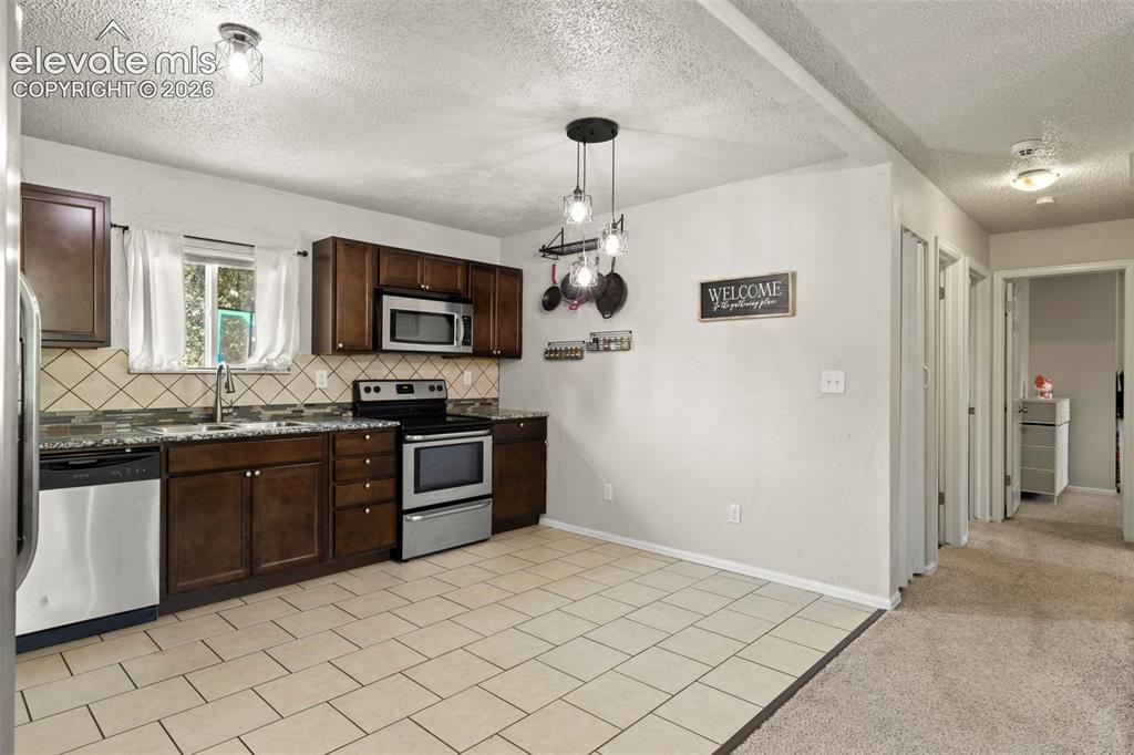 Image 10 of 30: Kitchen featuring stainless steel appliances, dark wood cabinetry, granite-
