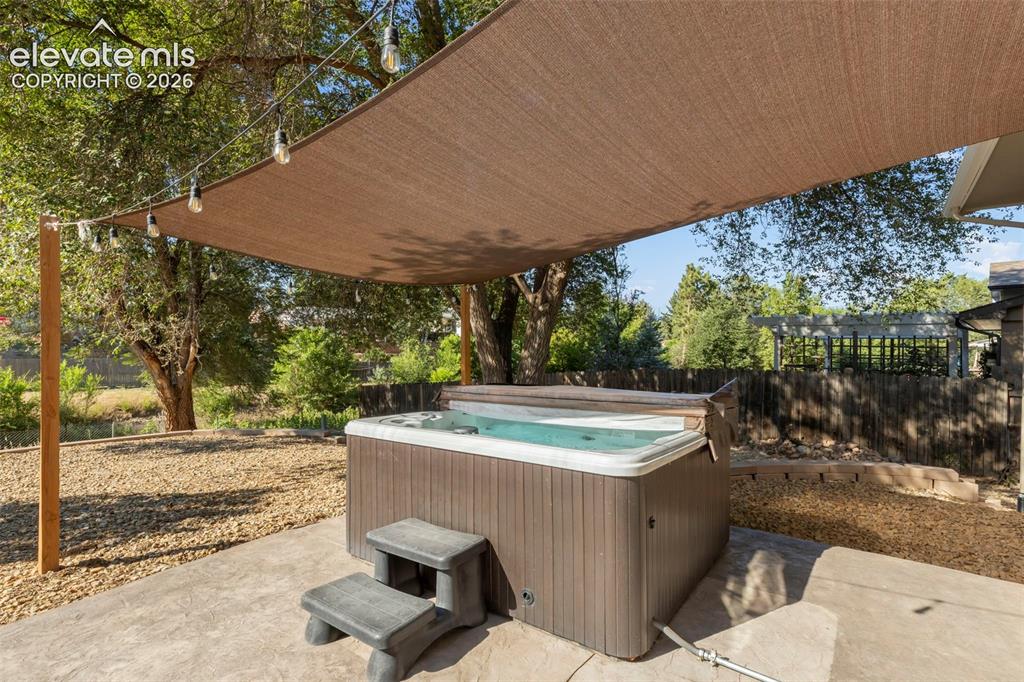 Image 30 of 30: Outdoor hot tub area featuring a shade sail canopy and string lighting over