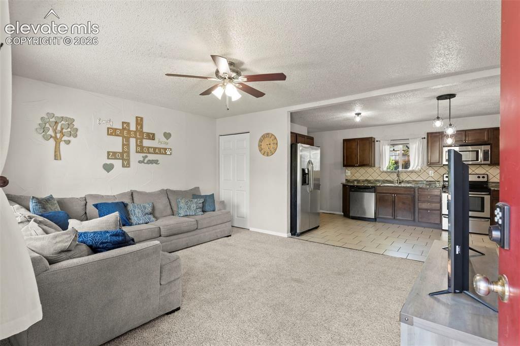 Image 4 of 30: Open-concept living area with carpeted flooring and ceiling fan