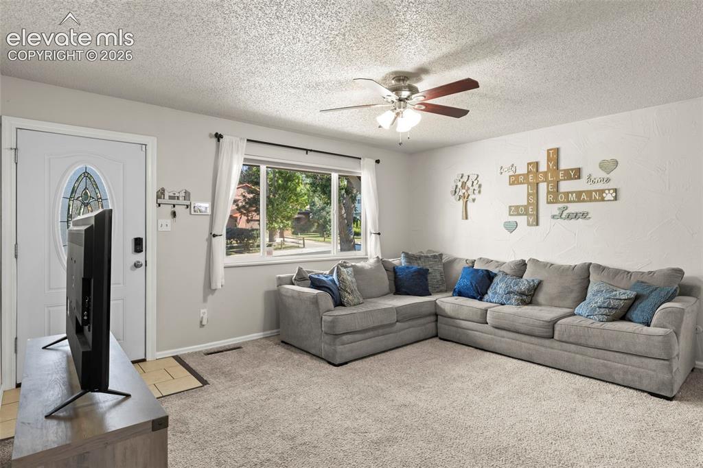 Image 5 of 30: Light-filled living area featuring a large picture window, textured ceiling