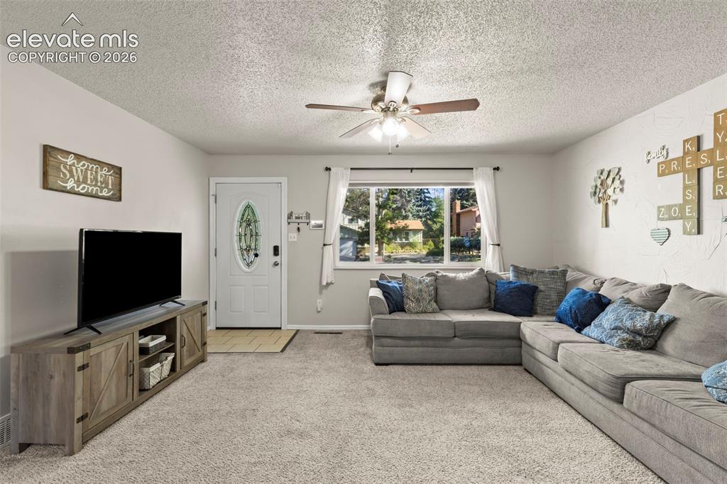 Image 6 of 30: Spacious living area featuring light-toned carpeting, a ceiling fan with in