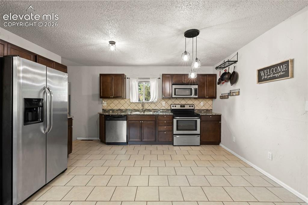Image 8 of 30: Kitchen featuring stainless steel appliances, dark wood cabinetry, and a pa