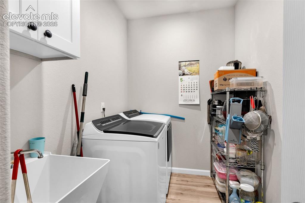 Image 26 of 49: Dedicated laundry area featuring a utility sink, upper cabinetry with black