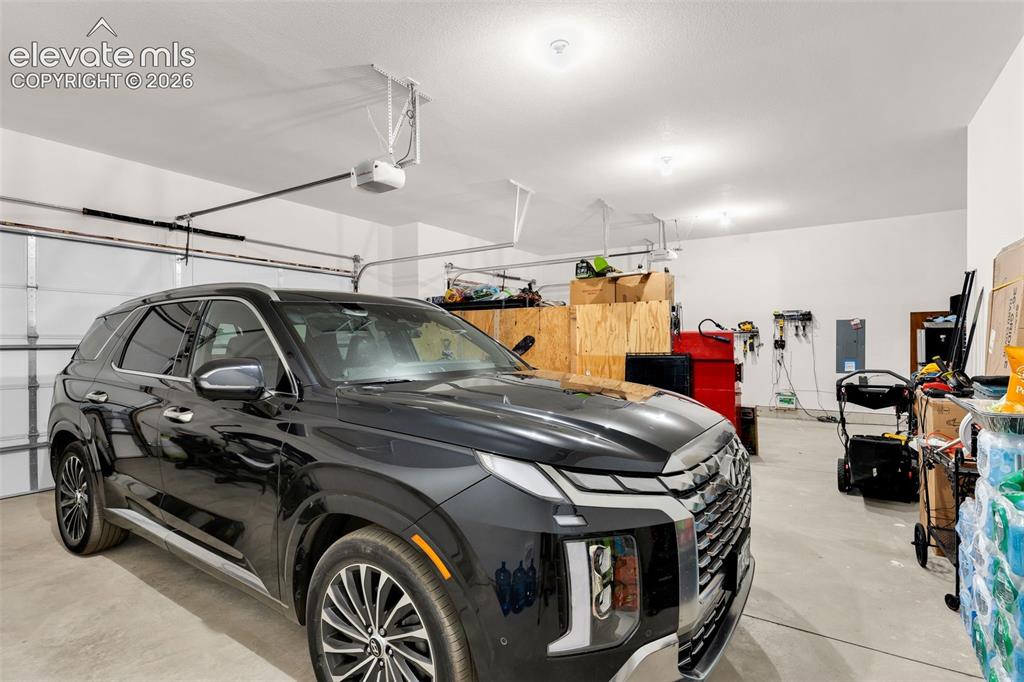 Image 28 of 49: Spacious garage featuring a concrete floor, white walls, multiple overhead