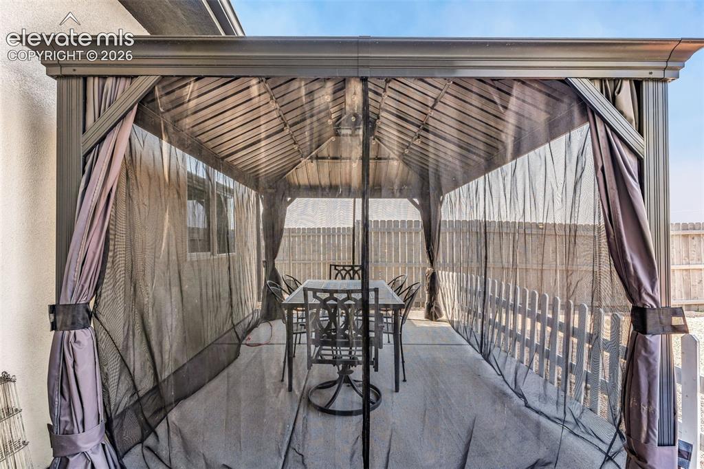 Image 31 of 49: Outdoor gazebo featuring a slatted roof, fabric privacy screens, and a conc