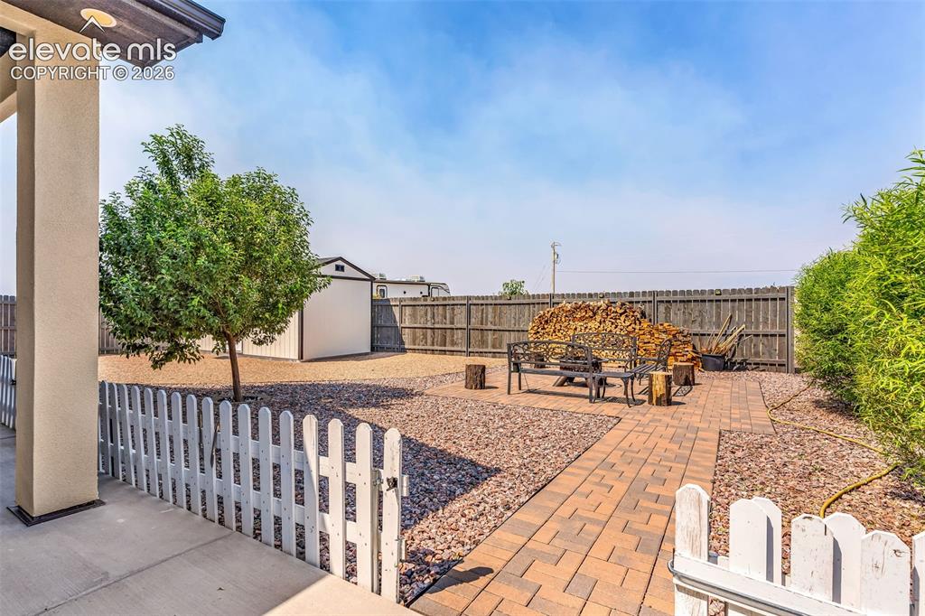 Image 33 of 49: Gravel backyard with a picket fence entry, paver pathway, and a detached st