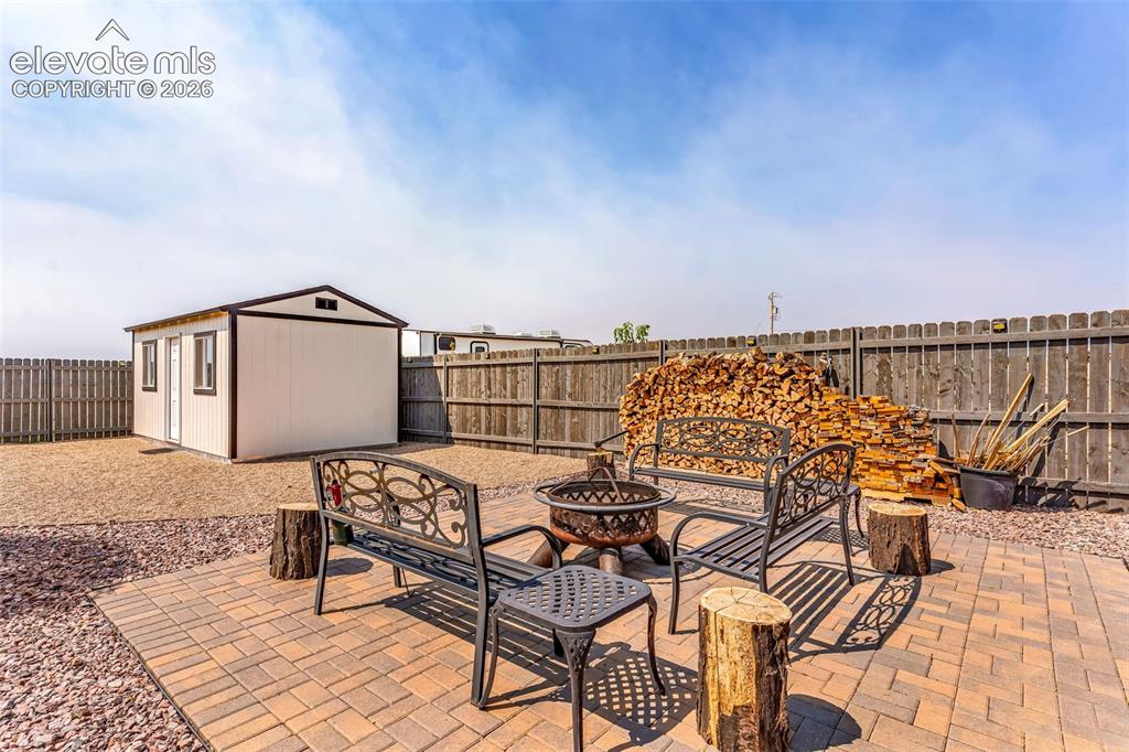 Image 34 of 49: Patio area featuring paver flooring, a fire pit, and a detached storage she