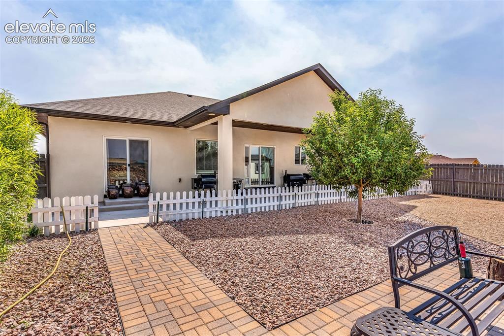 Image 35 of 49: Expansive backyard featuring a paver patio with a brick pathway, mature tre