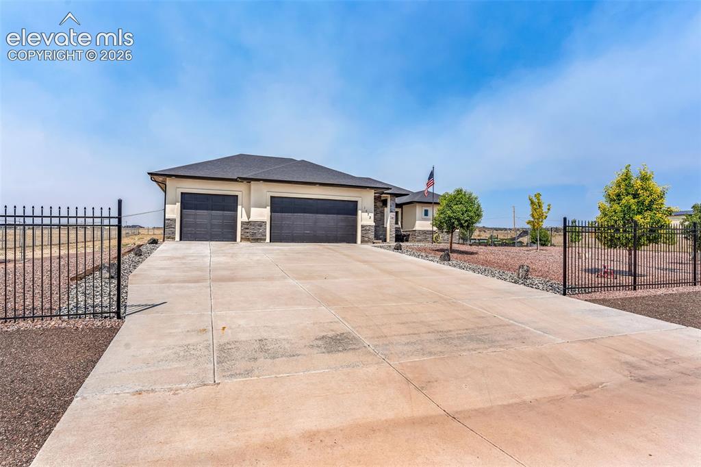 Image 5 of 49: Spacious concrete driveway leading to a two-car garage with dark paneled do