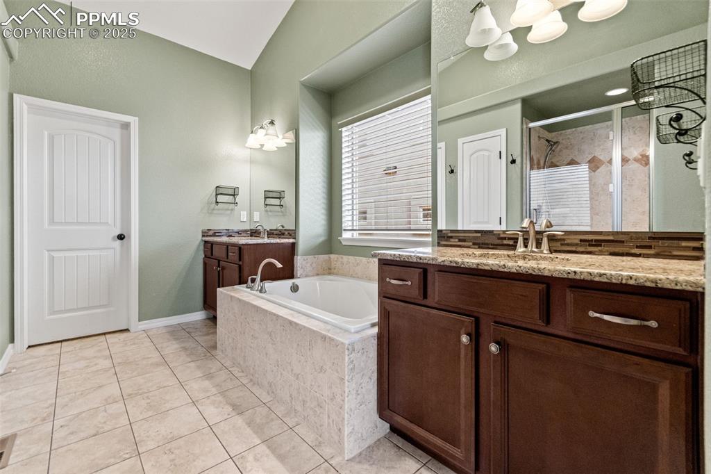 Image 27 of 45: Bathroom with light tile patterned flooring, a bath, two vanities, a stall 
