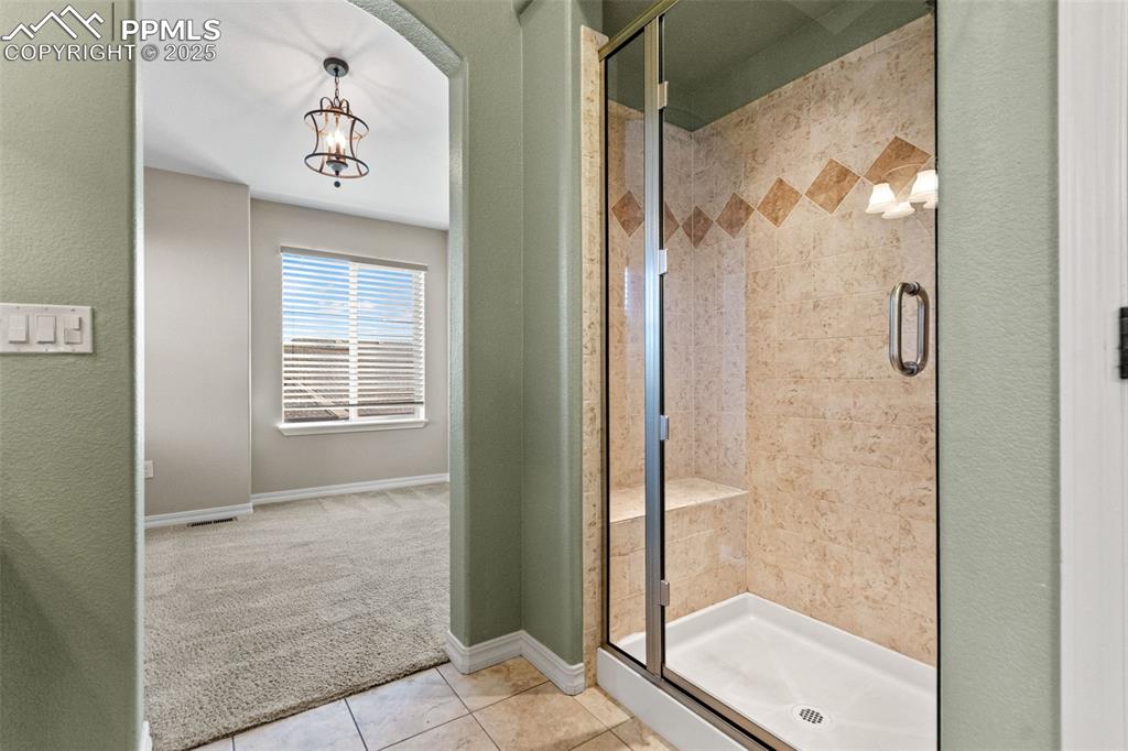 Image 28 of 45: Bathroom featuring a chandelier, carpet, a shower stall, tile patterned flo