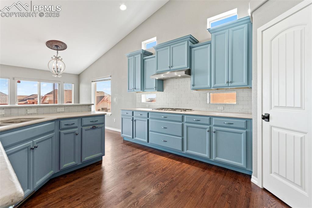 Image 7 of 45: Kitchen featuring backsplash, vaulted ceiling, blue cabinets, pendant light