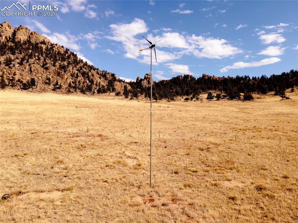 Image 43 of 43: Expansive land with a wind turbine, set against a backdrop of rocky hills a