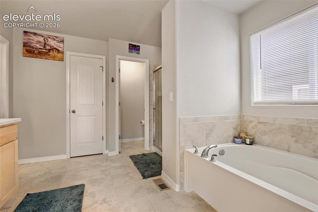 Image 26 of 33: Soaking tub with chrome fixtures, surrounded by light-toned tile wainscotin