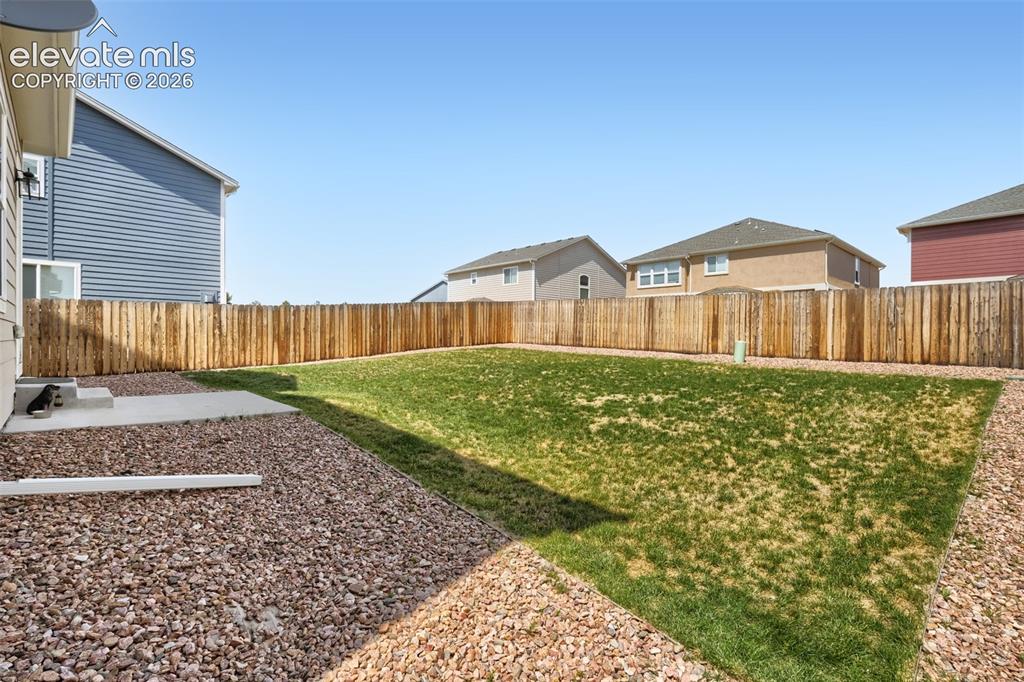 Image 29 of 33: Fenced backyard featuring a large grass lawn, gravel landscaping, and a con