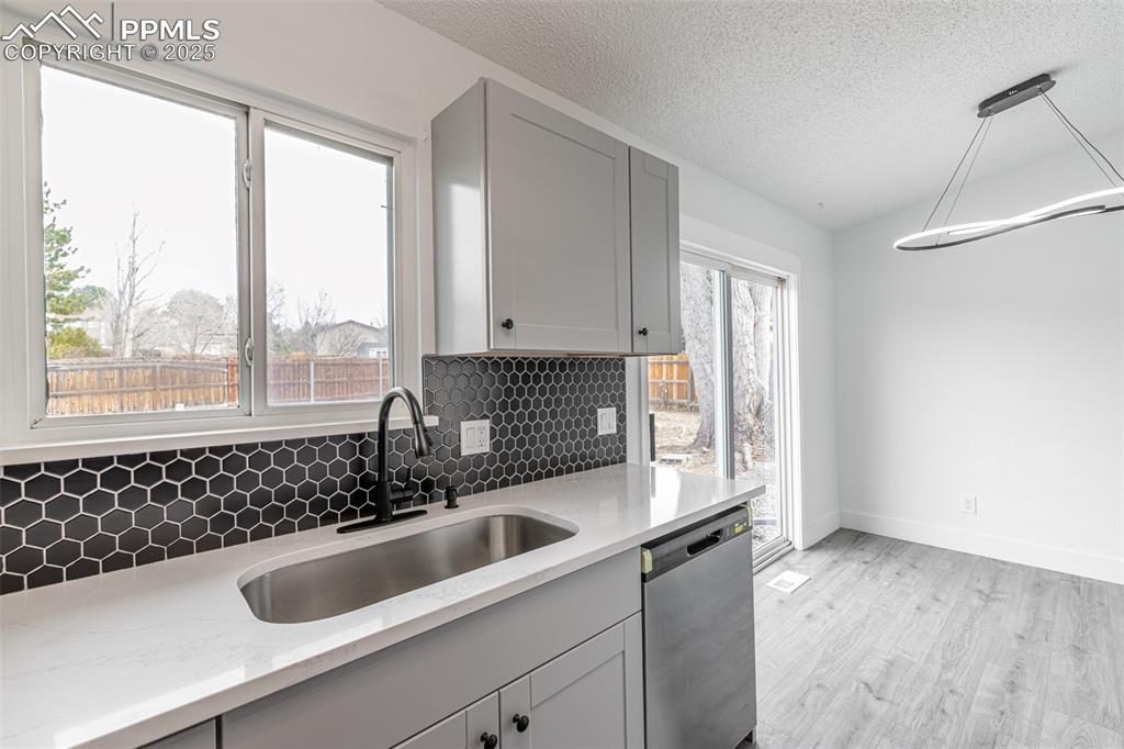 Image 11 of 33: Kitchen with backsplash, stainless steel dishwasher, light stone counters, 