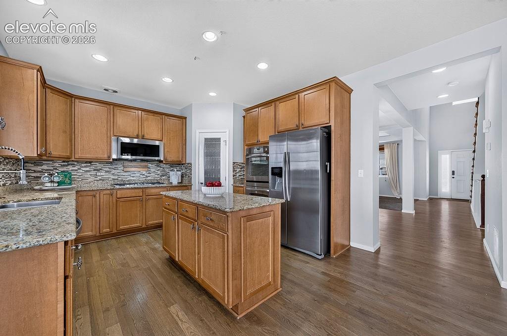 Image 17 of 50: Kitchen with wood-finish flooring, granite countertops, an island, and stai