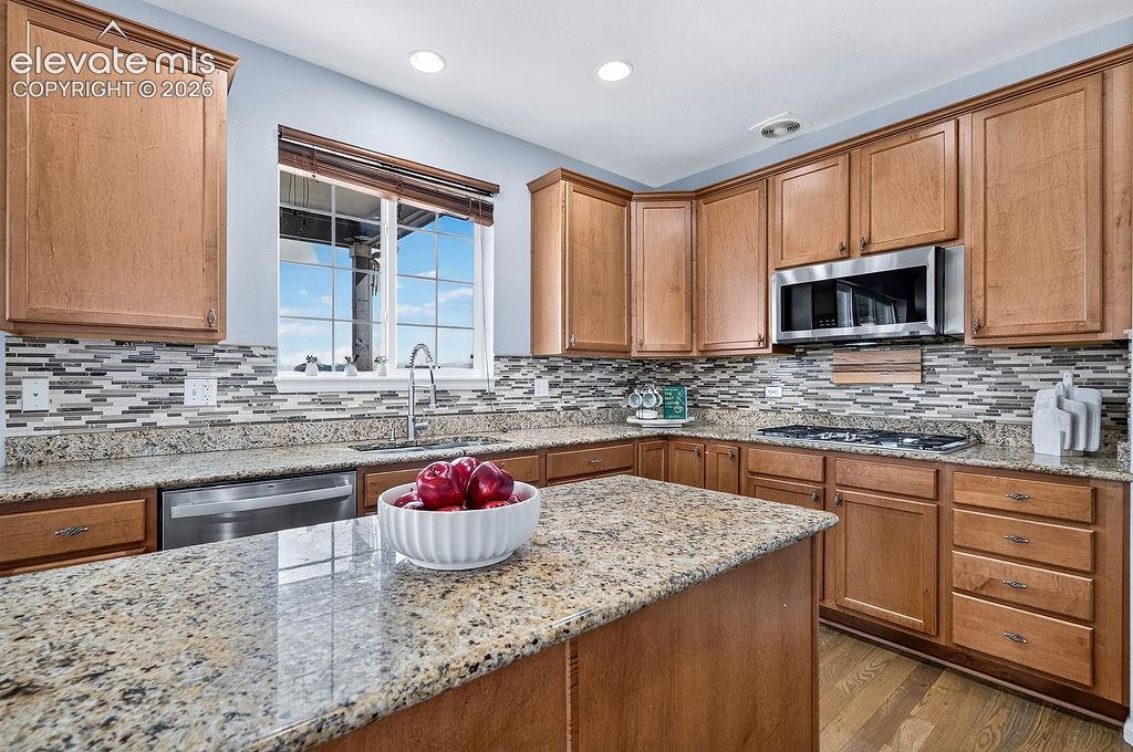 Image 18 of 50: Kitchen featuring wood cabinetry, granite countertops, tile backsplash, sta