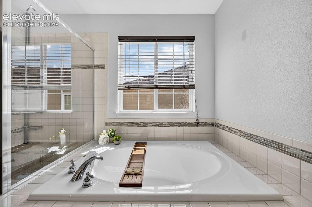 Image 30 of 50: Integrated soaking tub with chrome fixtures, tiled surround, and decorative