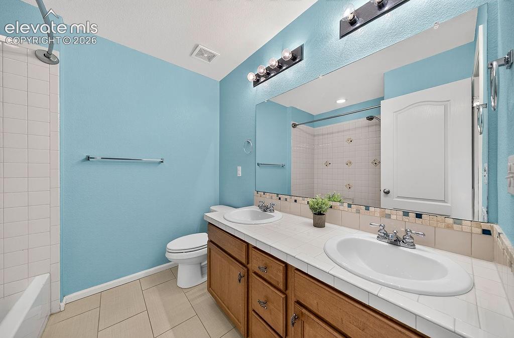 Image 34 of 50: Dual vanity with integrated sinks, wood-finish cabinetry, tile countertop, 