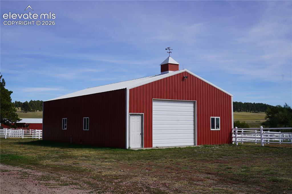 Image 34 of 41: Red metal-sided barn with a white roll-up garage door, white entry door, an
