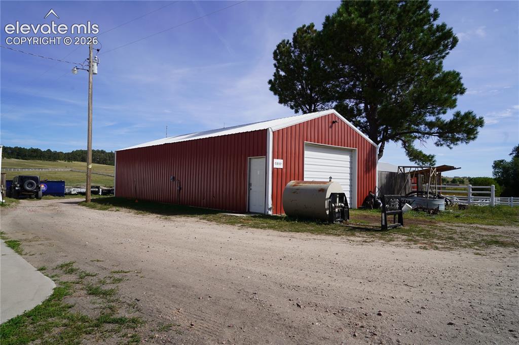 Image 37 of 41: Red metal building with white trim, a roll-up garage door, and a single ent