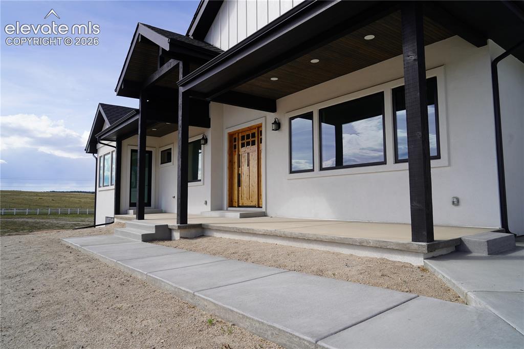 Image 9 of 41: White stucco exterior with black-framed windows, a wood-finish entry door,