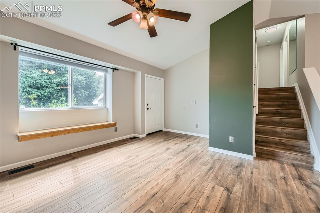 Image 5 of 32: Empty room with a ceiling fan, wood finished floors, vaulted ceiling, and s
