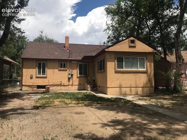 Image 18 of 18: Stucco exterior featuring a brown shingle roof, chimney, and multiple windo