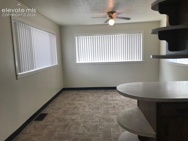 Image 7 of 18: Spacious room featuring multiple windows with vertical blinds, textured cei